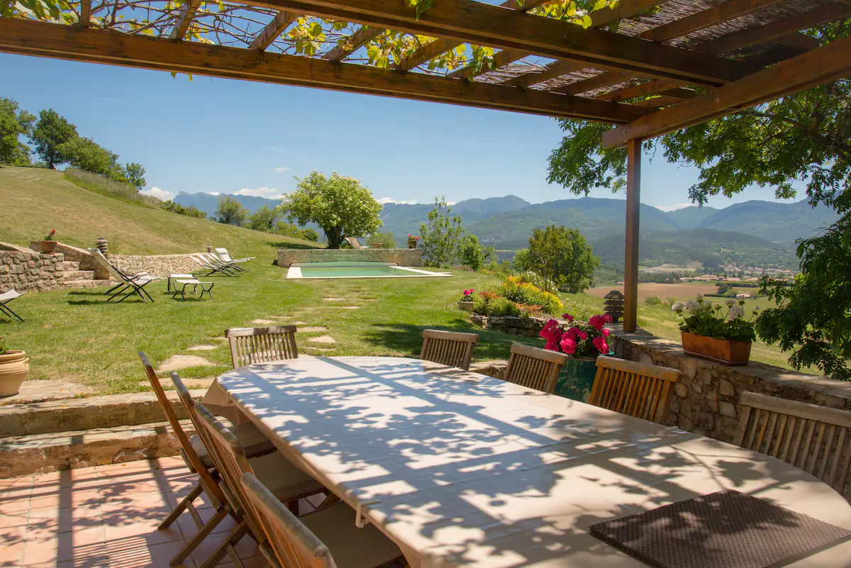 Shaded terrace under the pergola, table set facing the pool and the mountains